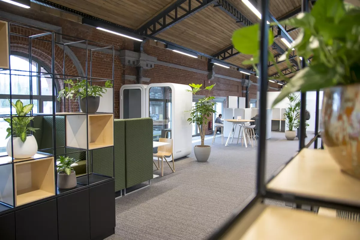 Bureau moderne dans un bâtiment en briques avec cabines acoustiques, plantes et plafond industriel. 