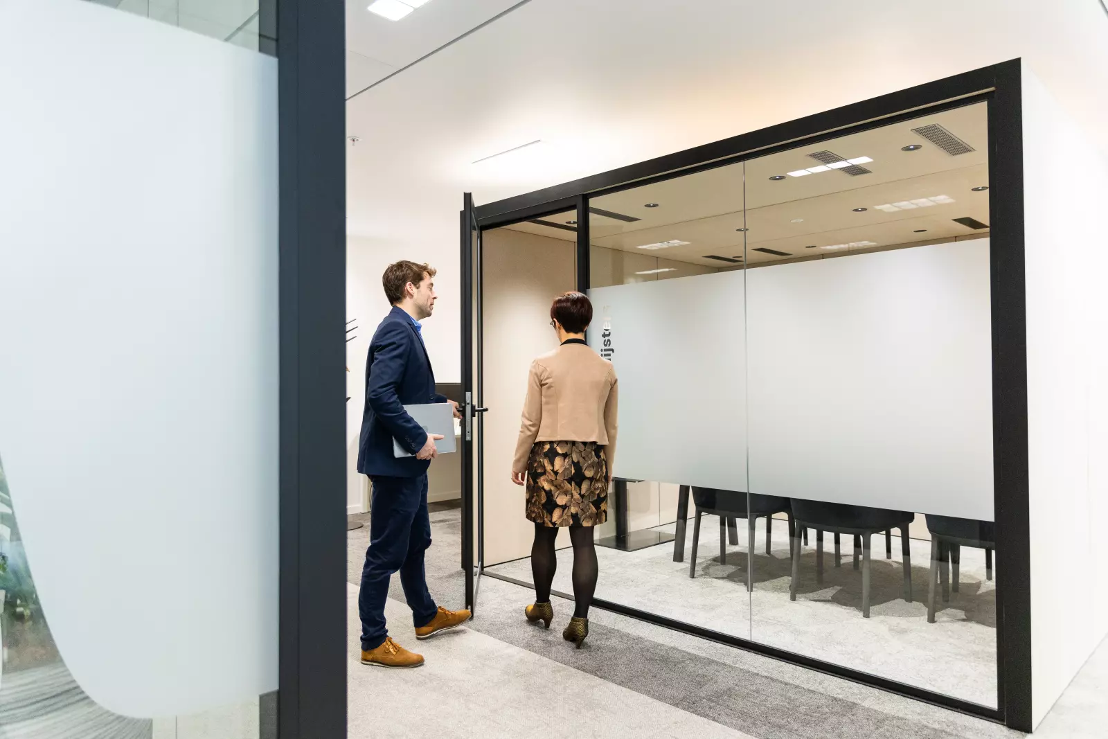 Zwei Kollegen betreten einen Besprechungsraum mit Glaswänden in einem modernen Büro.