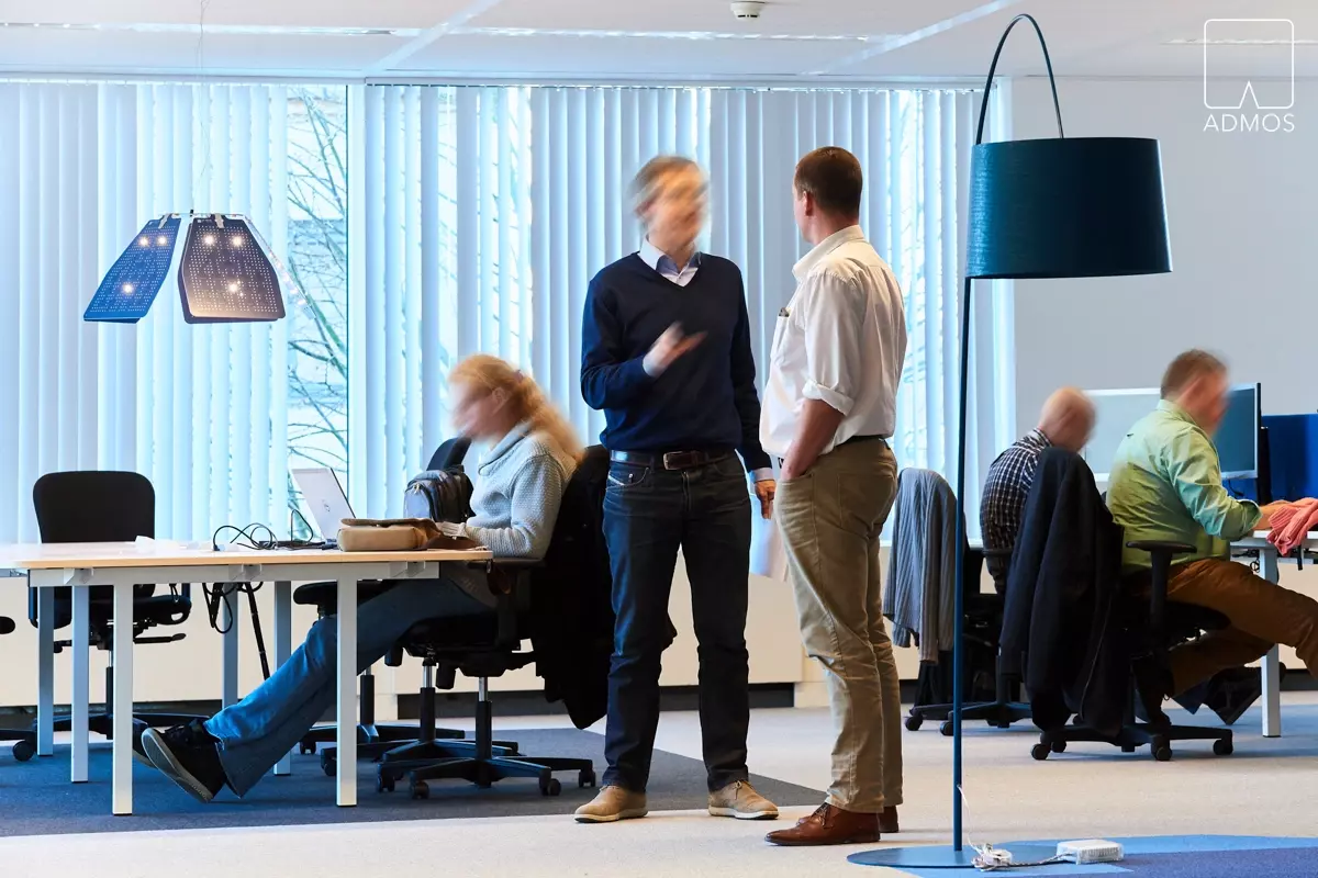 Bureau moderne avec employés travaillant et discutant, lampes design bleues et bureaux blancs.